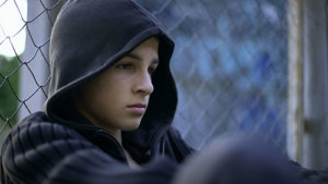 teen with hood up leans against fence at a mood disorder treatment center