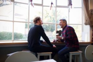 two men talk near a window in a men's rehab program